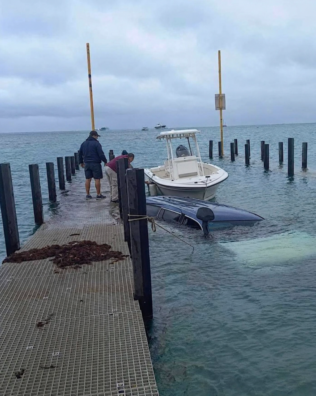 Two boaters on a launch dock beside a submerged pickup truck and a small center-console boat.