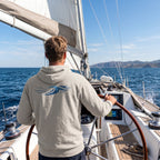 Deepwater Crew Co. beige hooded long sleeve tee with blue wave graphic worn by a man sailing on a boat.