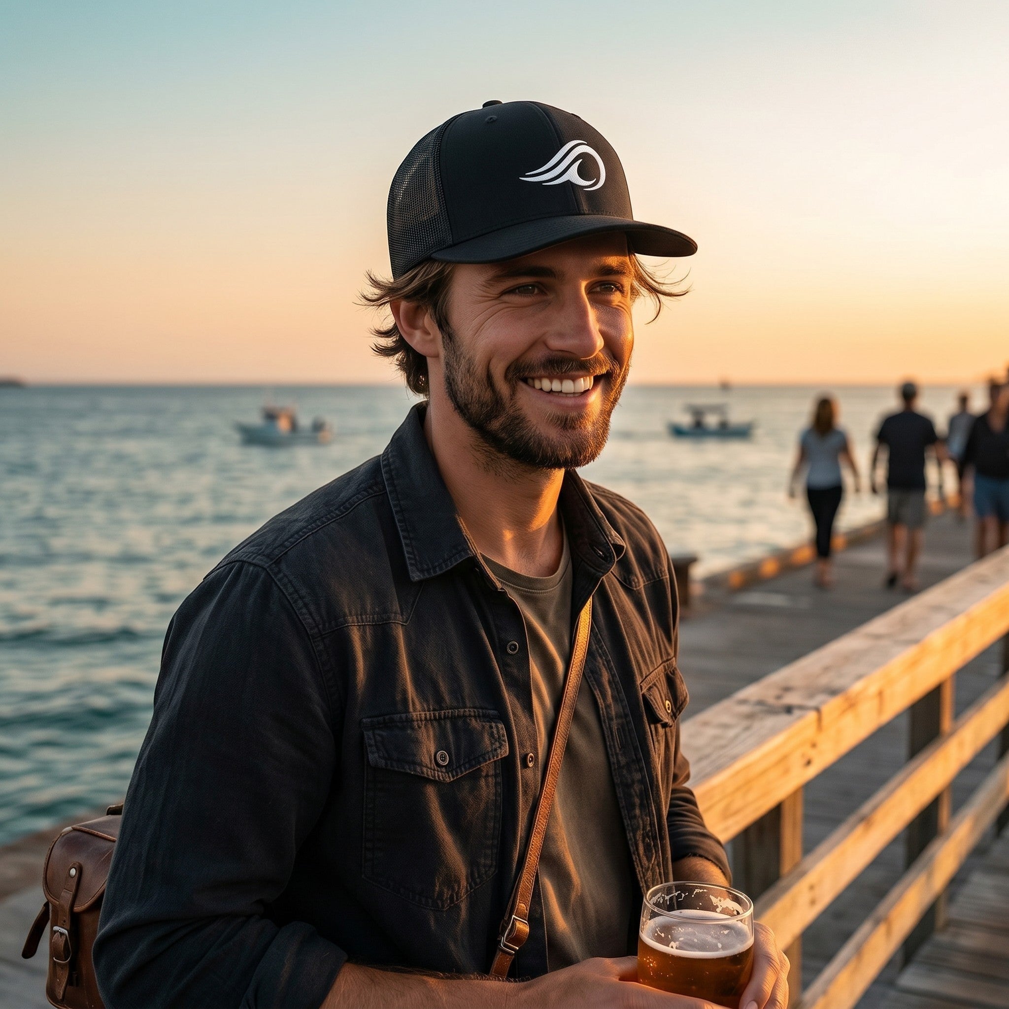 Deepwater Crew Co. black trucker cap with white wave logo worn by a smiling man on a pier at sunset.