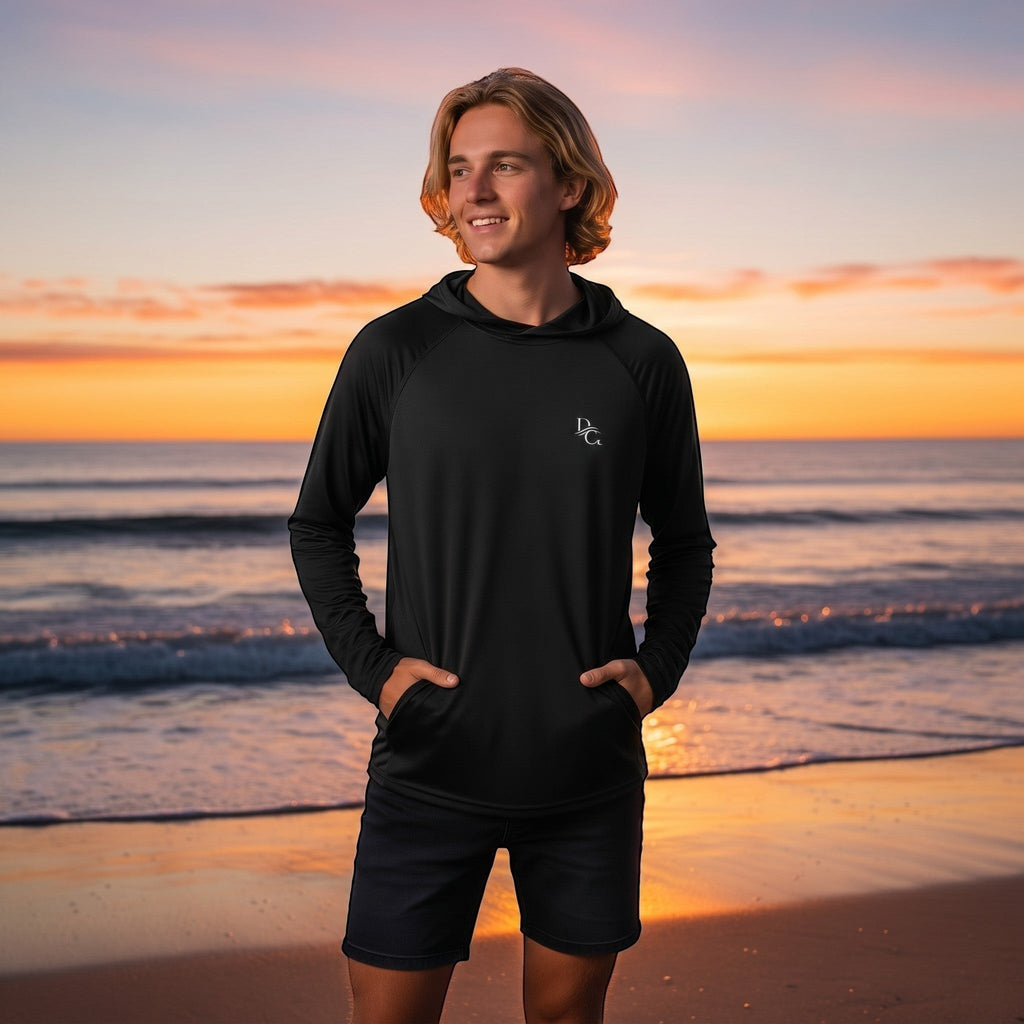 Deepwater Crew Co. man wearing a black performance UPF hoodie with raglan sleeves on a beach at sunset