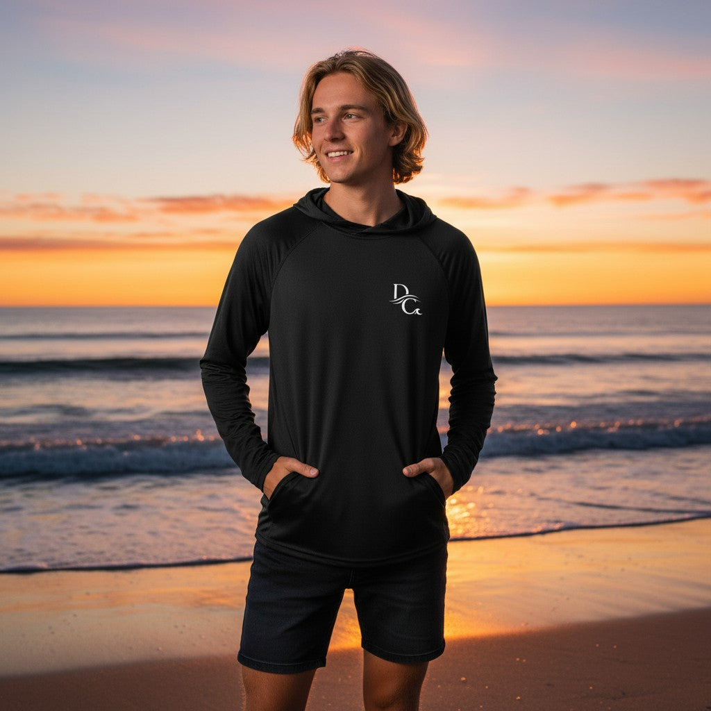 Man wearing a black Deepwater Crew Co. long-sleeve performance UV hoodie on a beach at sunset.