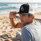 Deepwater Crew Co. black and white 5-panel trucker cap with flat bill and embroidered logo worn by a man on the beach.