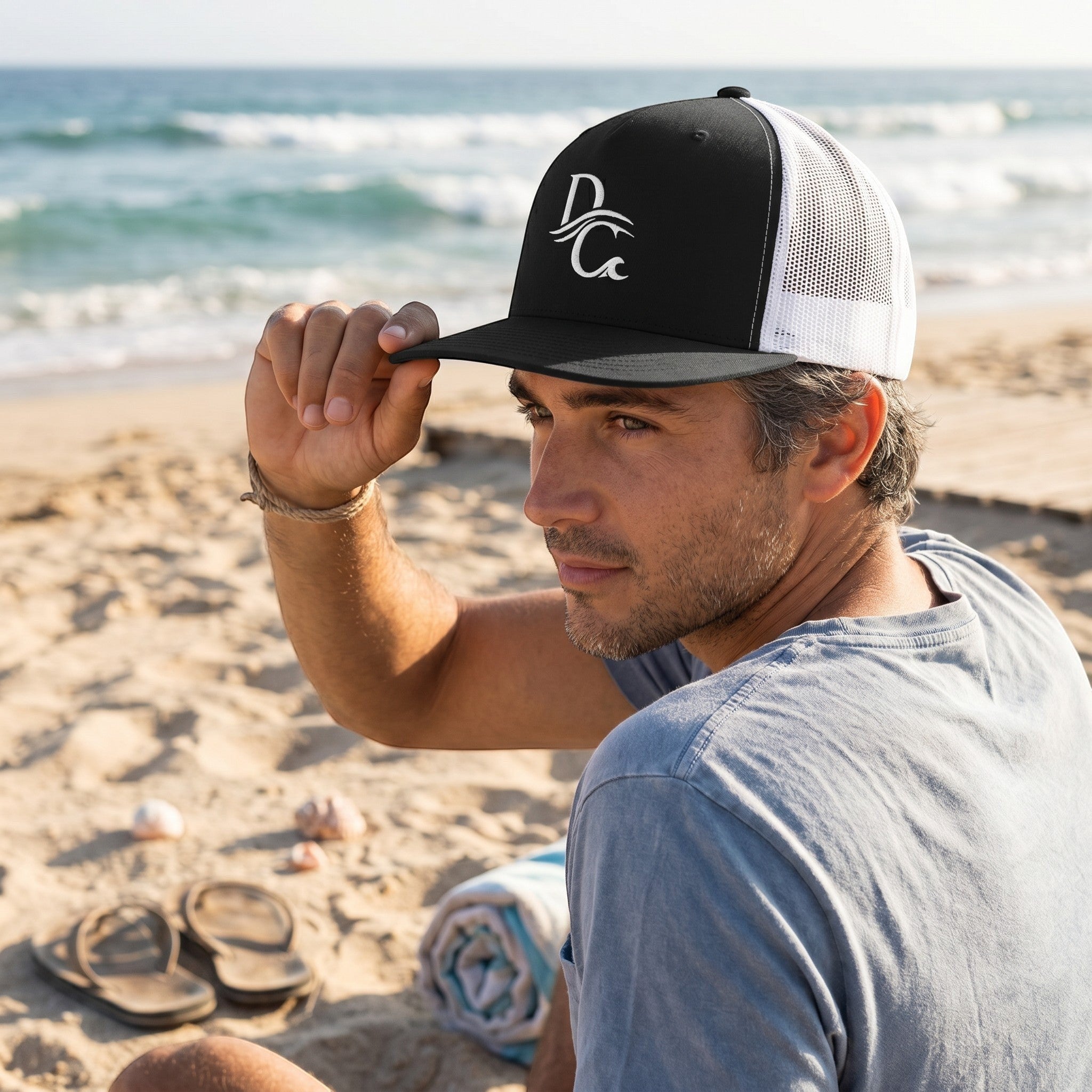 Deepwater Crew Co. black and white 5-panel trucker cap with flat bill and embroidered logo worn by a man on the beach.