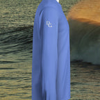 Deepwater Crew Co. blue long sleeve hooded t-shirt with white logo on sleeve, side view against ocean wave background.