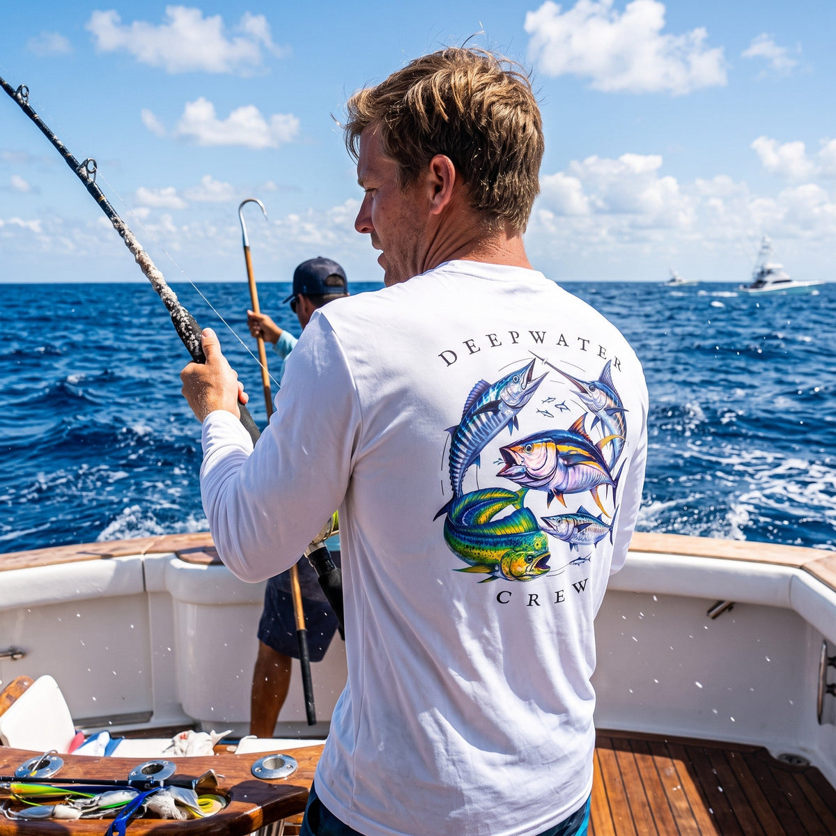 Man wearing a white Deepwater Crew Co. Bluewater Strike UPF 44+ long-sleeve performance shirt, back view with colorful pelagic game fish collage and Deepwater Crew lettering while offshore fishing.