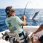 Man wearing a Dusty Blue Deepwater Crew Co. Called to Fish T-shirt, back view while offshore fishing from a boat.