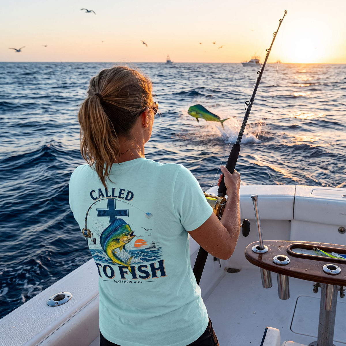 Woman wearing a Mint Deepwater Crew Co. Called to Fish T-shirt, back view while fishing from a boat at sunset.