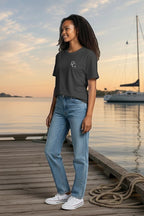 Woman wearing a Deepwater Crew Co. charcoal grey cotton t-shirt with a small logo on a wooden dock by the ocean.