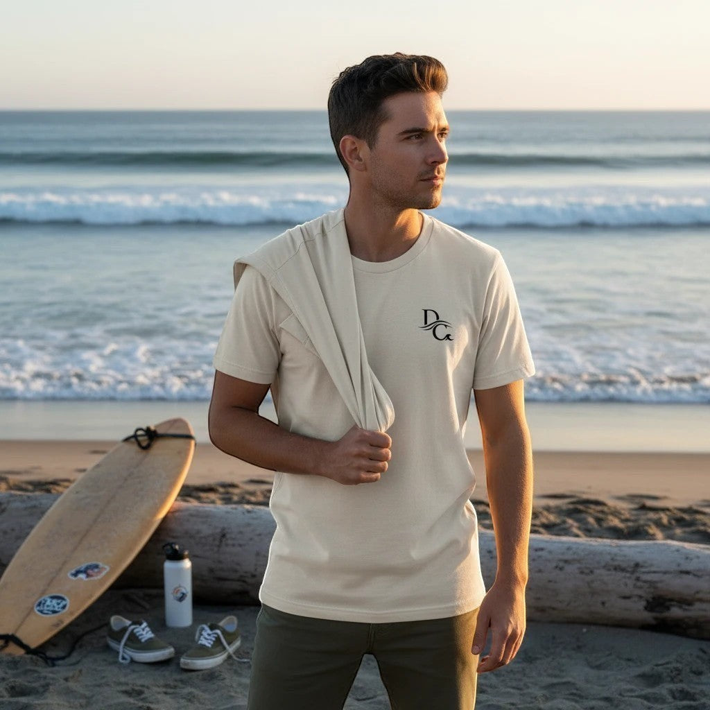 Deepwater Crew Co. cream cotton crew neck t-shirt with small logo on chest, worn by a man on a beach at sunset.