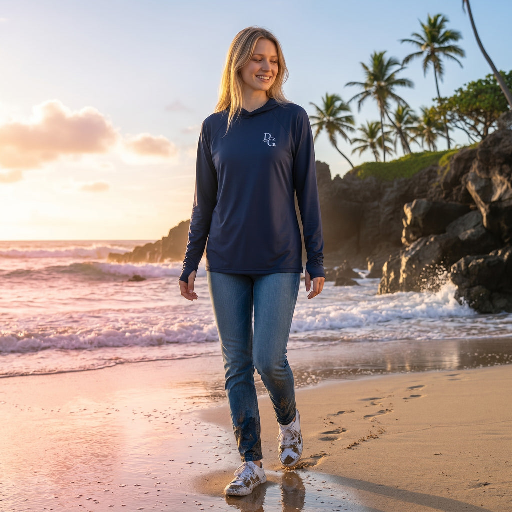 Deepwater Crew Co. dark blue long-sleeve UV performance hoodie worn by a woman walking on a beach at sunset.