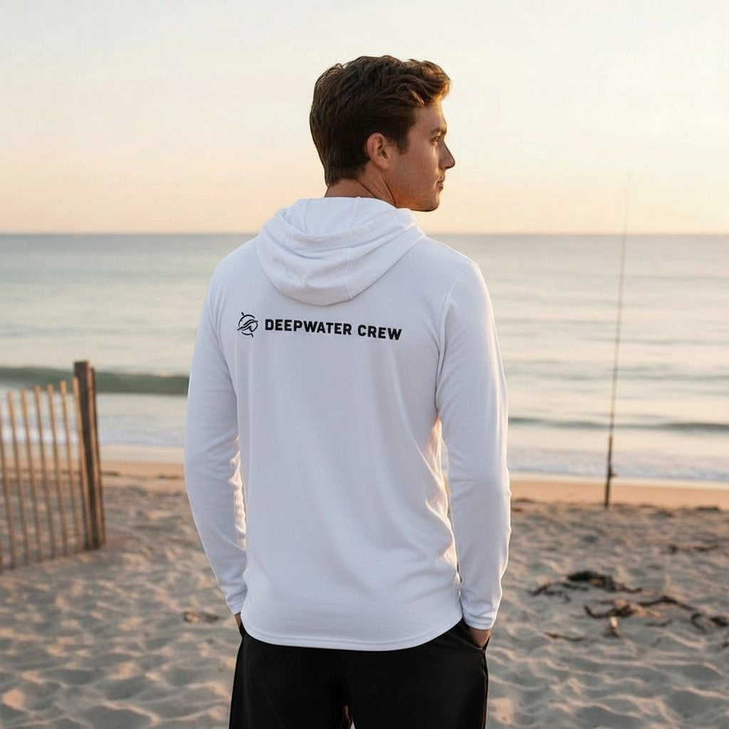 Deepwater Crew Co. dark grey tri-blend long-sleeve hooded tee with chest logo, worn by a man on a beach at sunset.