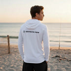 Deepwater Crew Co. dark grey tri-blend long-sleeve hooded tee with chest logo, worn by a man on a beach at sunset.