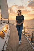 Deepwater Crew Co. dark grey crew neck t-shirt with small white logo on chest, worn by a woman on a sailboat deck at sunset.