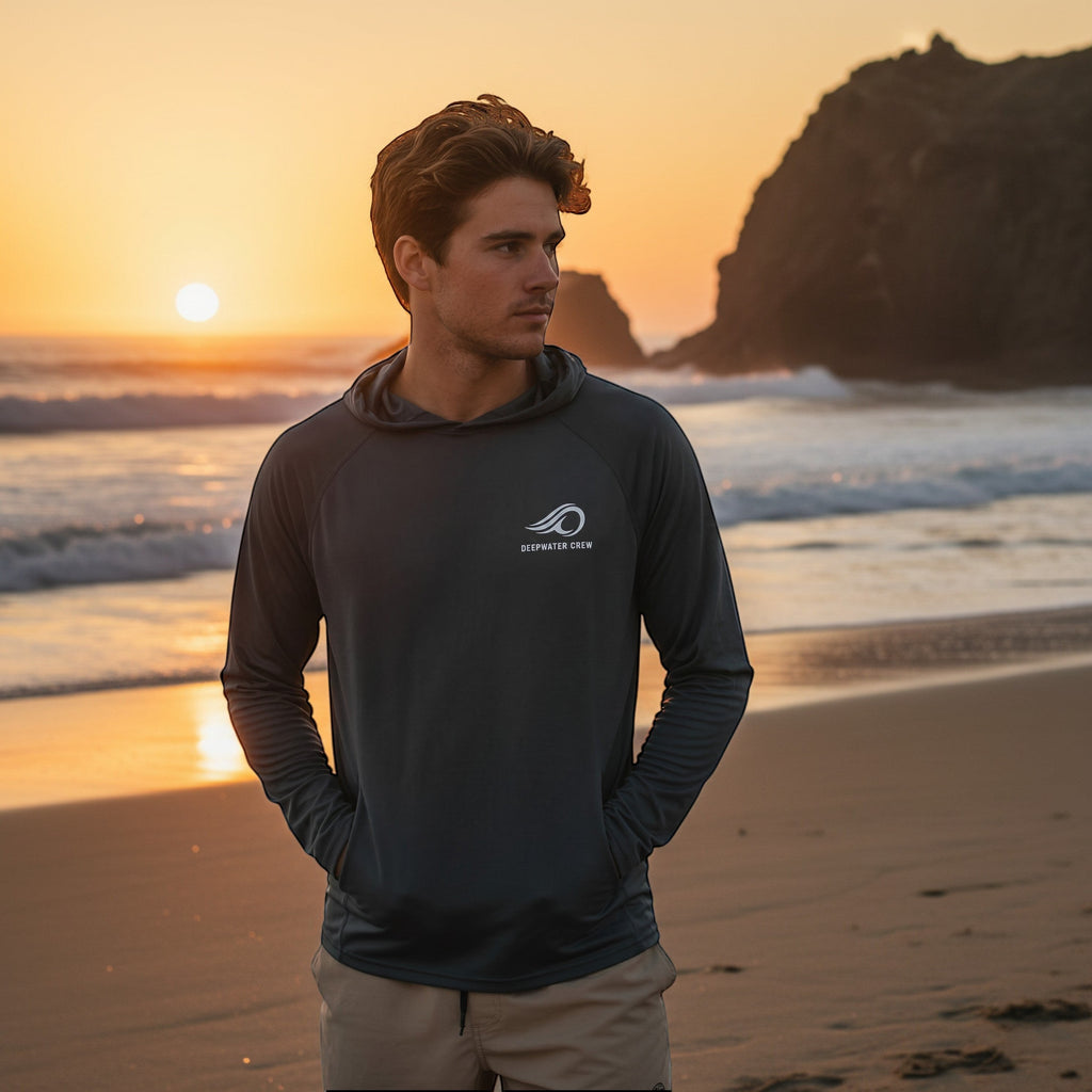 Deepwater Crew Co. dark grey performance UPF hoodie worn by a man on a beach at sunset with raglan sleeves.