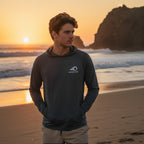 Deepwater Crew Co. dark grey performance UPF hoodie worn by a man on a beach at sunset with raglan sleeves.