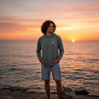 Deepwater Crew Co. dark grey performance UPF hoodie worn by a man standing on a beach at sunset.