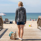 Woman wearing a dark grey Deepwater Crew Co. long-sleeve performance UV hoodie standing on a beach boardwalk.