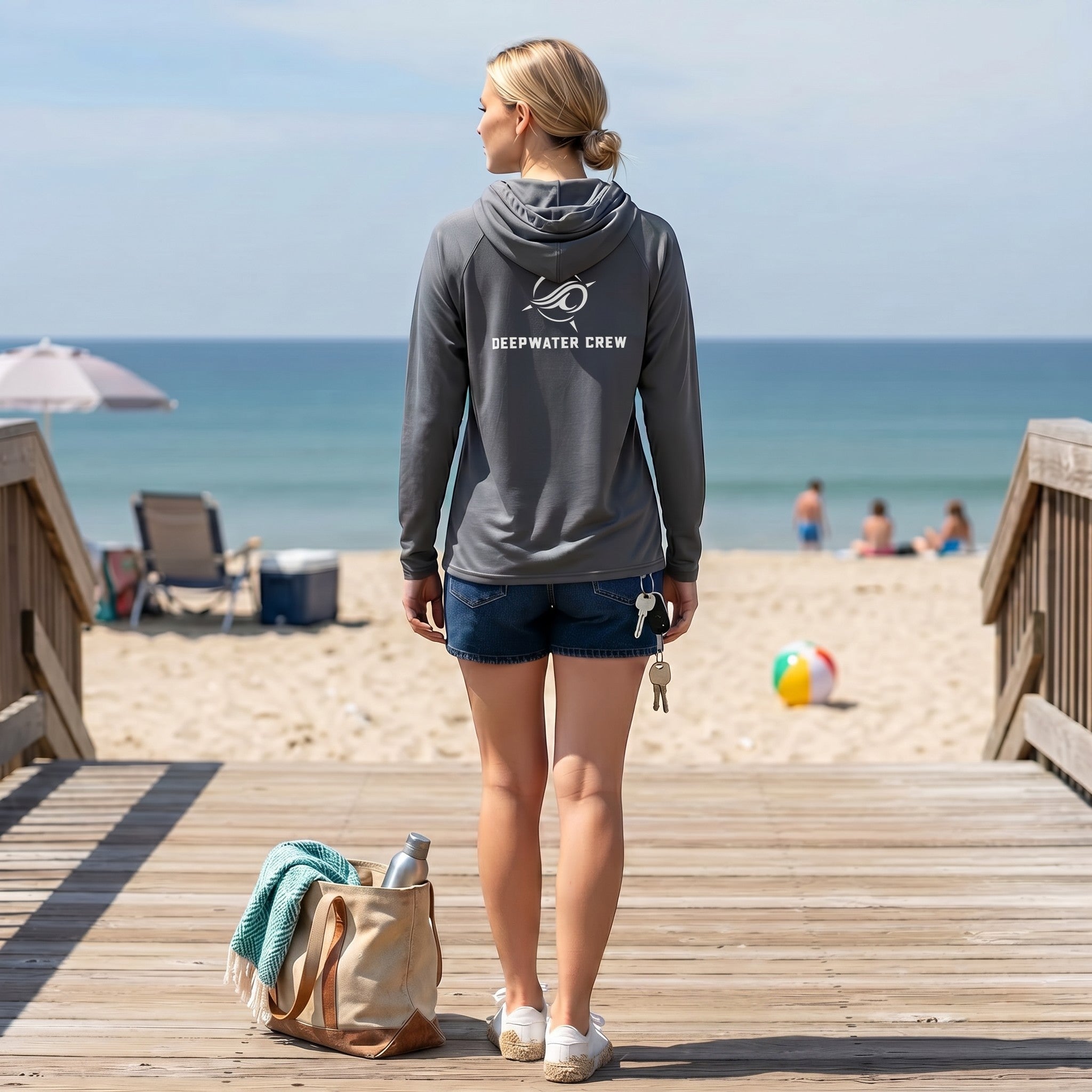 Woman wearing a dark grey Deepwater Crew Co. long-sleeve performance UV hoodie standing on a beach boardwalk.