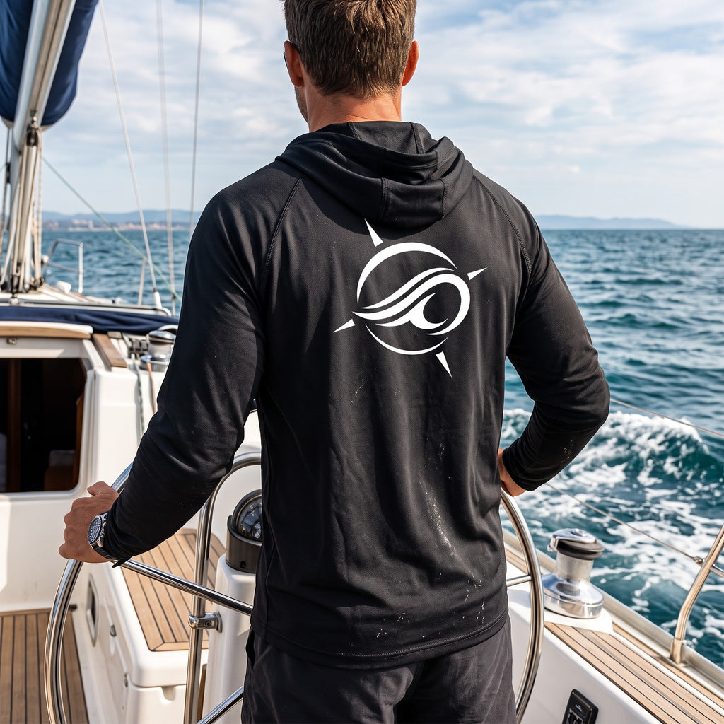 Deepwater Crew Co. dark performance sun hoodie with white logo on back, worn by a man steering a sailboat at sea.