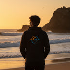 Deepwater Crew Co. dark performance UPF hoodie with a back compass logo, worn by a man at sunset on the beach.