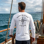 Man wearing a white Deepwater Crew Co. Deepwater Nomad UPF 44+ long-sleeve performance shirt, back view with distressed compass rose graphic while sailing on open water.