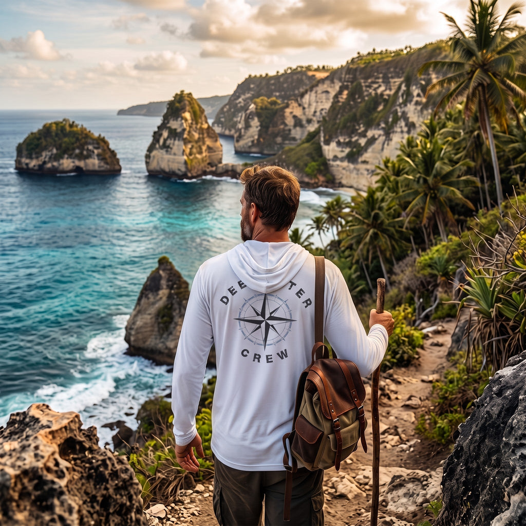 Man wearing a white Deepwater Crew Co. Deepwater Nomad UPF 50+ performance hoodie, back view with distressed compass rose graphic while hiking along a tropical coastline.