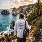 Man wearing a white Deepwater Crew Co. Deepwater Nomad UPF 50+ performance hoodie, back view with distressed compass rose graphic while hiking along a tropical coastline.