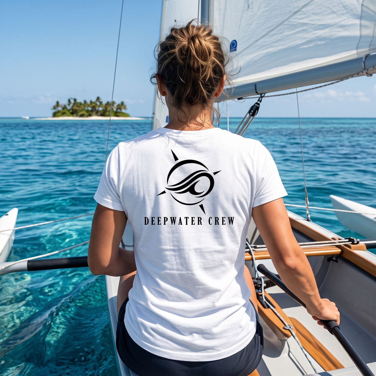Woman wearing a white Deepwater Crew Co. Flagship crewneck T-shirt, back view with compass-and-wave emblem and Deepwater Crew lettering while sailing on tropical waters.