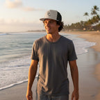 Deepwater Crew Co. flat bill trucker cap with mesh back worn by a man on a beach at sunset.