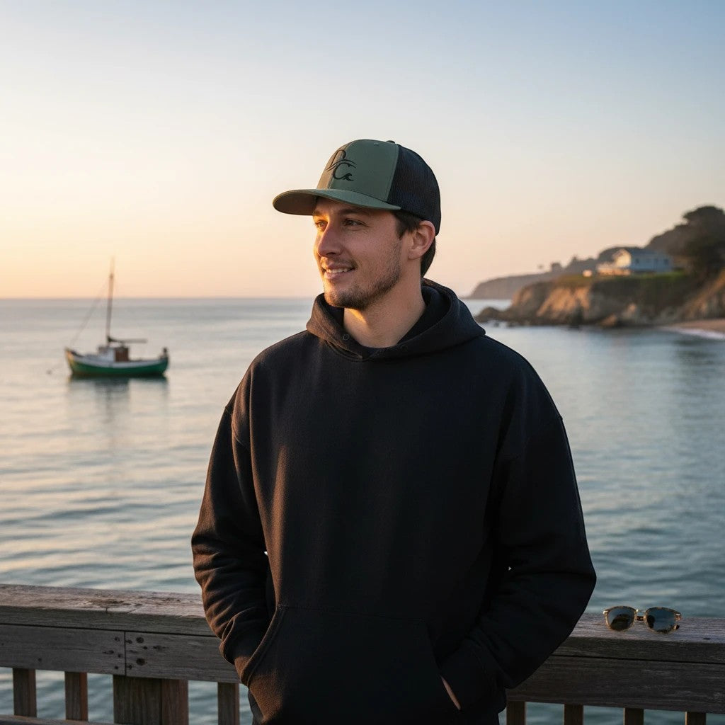 Deepwater Crew Co. green and black trucker hat with embroidered logo, worn by a man on a pier at sunset.