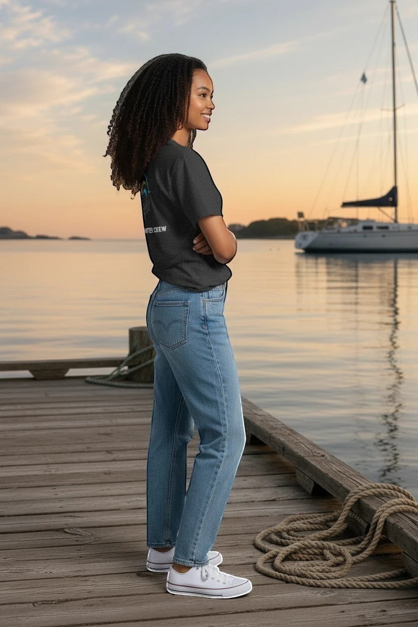 A woman wearing a Deepwater Crew Co. dark grey cotton t-shirt with back graphic, standing on a wooden dock at sunset.