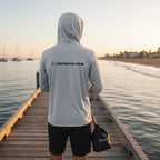 Deepwater Crew Co. light grey hooded long-sleeve tee with chest logo, worn by a man fishing on a pier at sunset.