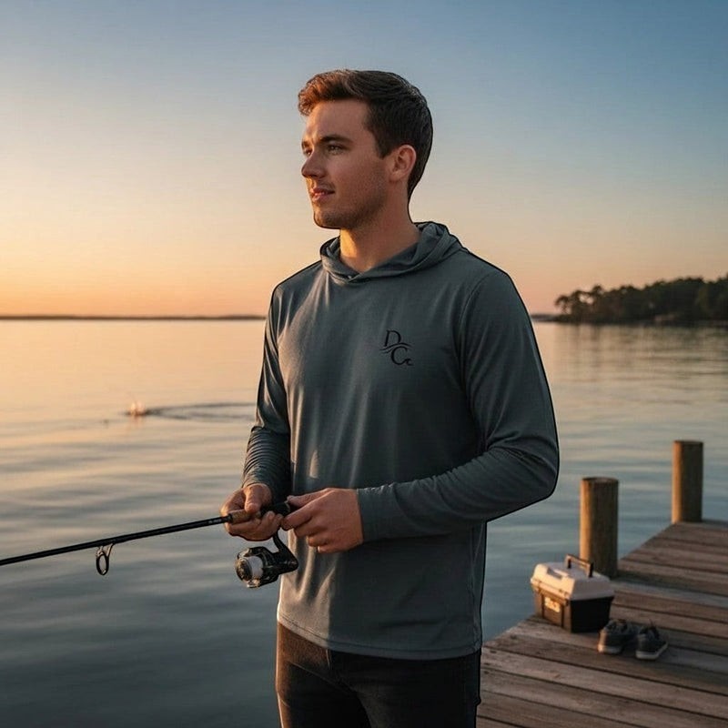 Man wearing a Deepwater Crew Co. grey long sleeve hooded tee with chest logo while fishing on a wooden dock at sunset.