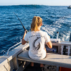 Woman wearing a white Deepwater Crew Co. Hooked graphic t-shirt while fishing from a boat on the open ocean.