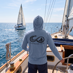 Man wearing a Saltwater Deepwater Crew Co. Keep Sailing cotton hooded long-sleeve T-shirt, back view with infinity-style ocean wave and sailboat graphic above Deepwater Crew lettering while sailing.