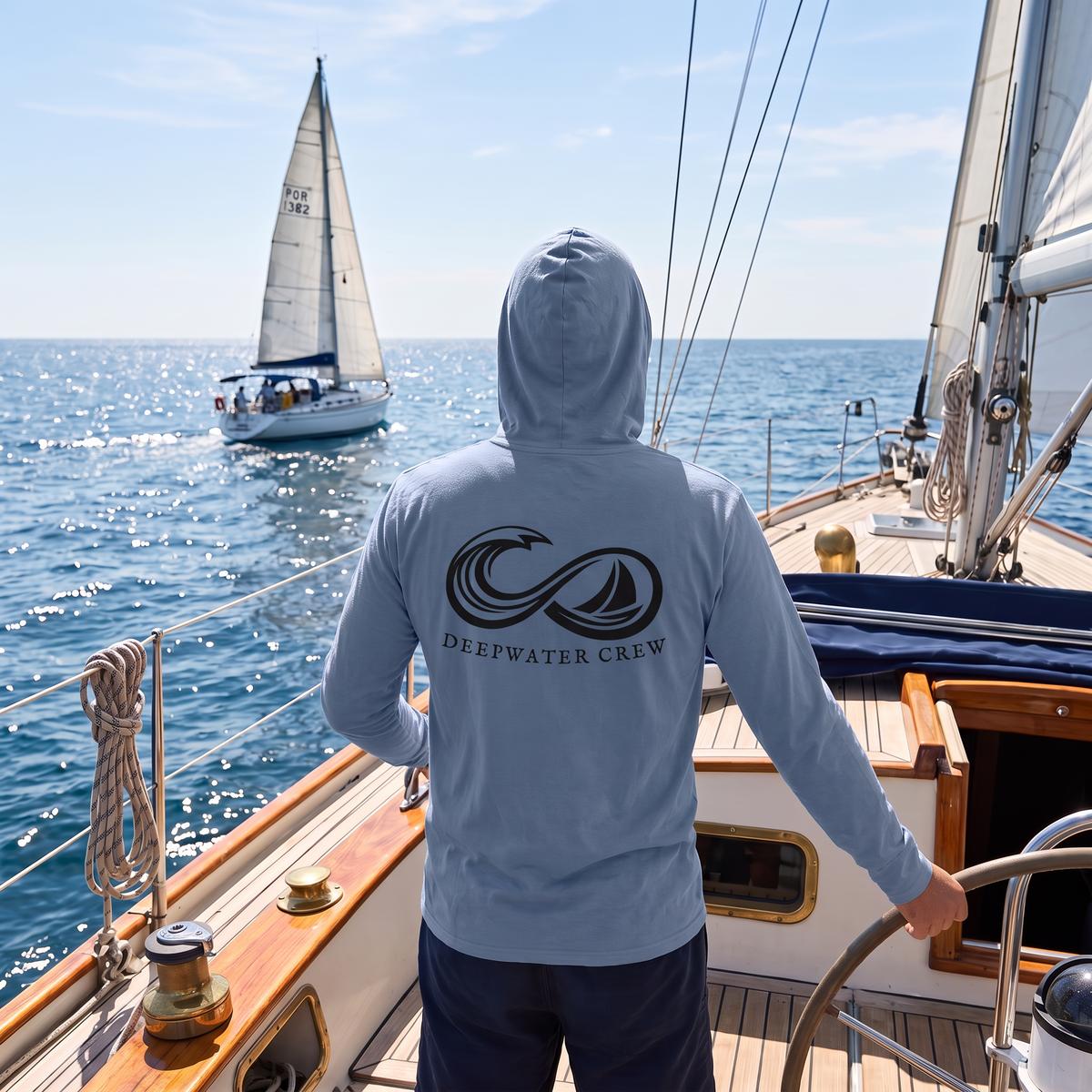 Man wearing a Saltwater Deepwater Crew Co. Keep Sailing cotton hooded long-sleeve T-shirt, back view with infinity-style ocean wave and sailboat graphic above Deepwater Crew lettering while sailing.