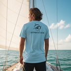 Deepwater Crew Co. light blue cotton crew neck t-shirt with a nautical logo on the back, worn by a man on a sailboat.