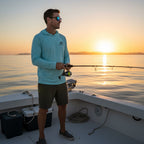 Deepwater Crew Co. man wearing a light blue performance UV hoodie while fishing on a boat at sunset