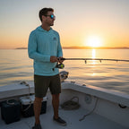 Deepwater Crew Co. man wearing a light blue performance UPF hoodie while fishing on a boat at sunset