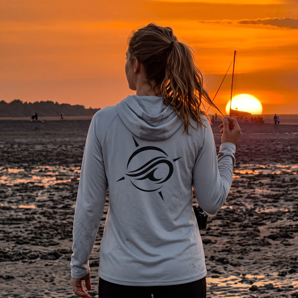 Woman wearing a Deepwater Crew Co. light grey UPF 44+ performance hoodie with a logo on the back at sunset