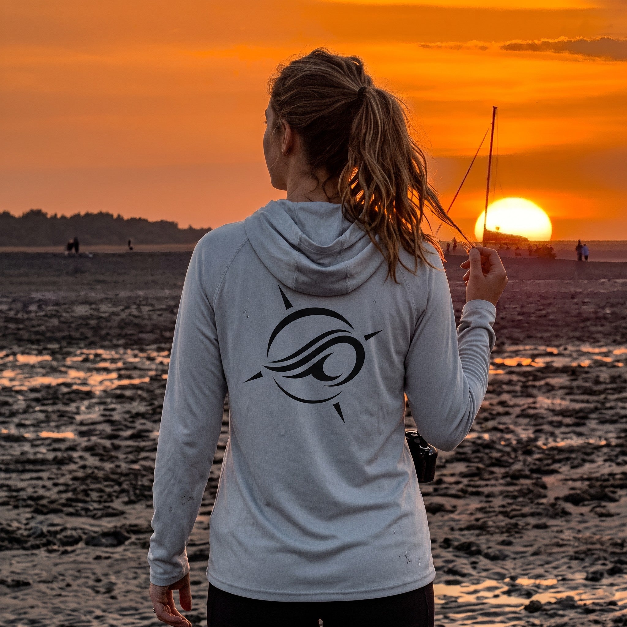 Woman wearing a Deepwater Crew Co. light grey UPF 44+ performance hoodie with a logo on the back at sunset