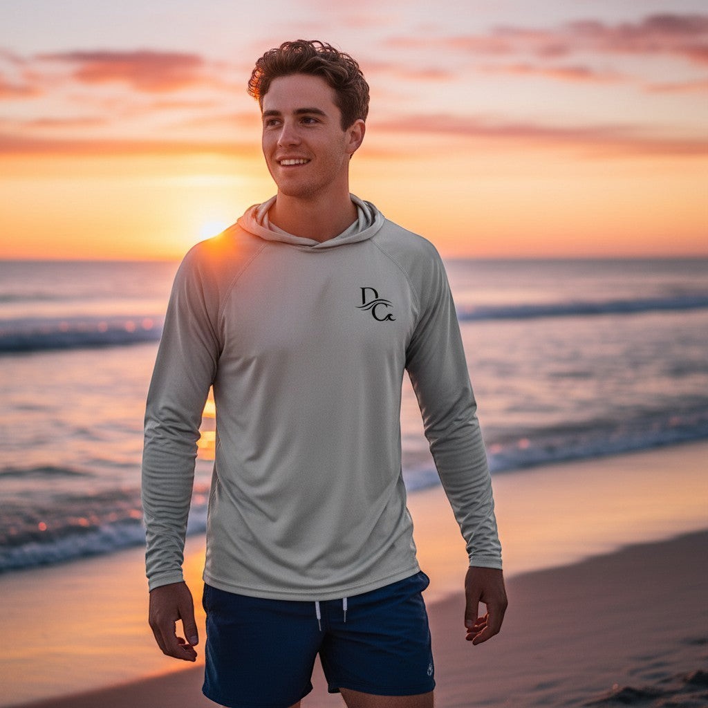 Man wearing a Deepwater Crew Co. light grey UV performance hoodie on a beach at sunset with raglan sleeves.