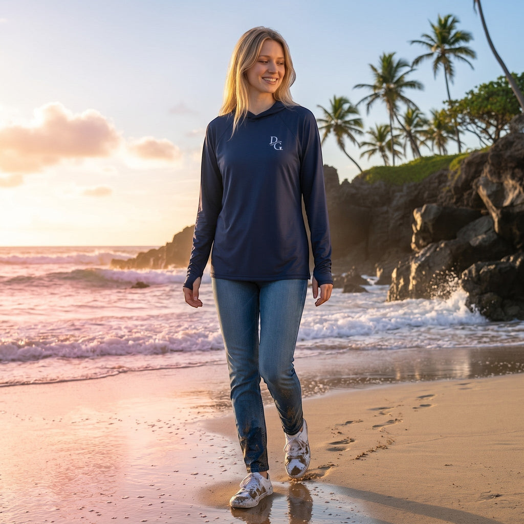 Deepwater Crew Co. woman wearing a dark navy long-sleeve performance UV hoodie on a beach at sunset.
