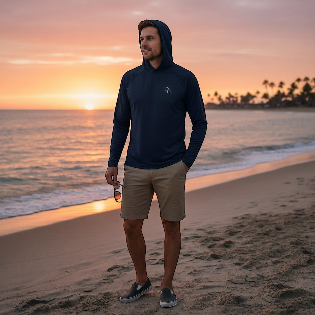 Deepwater Crew Co. man wearing a dark navy performance UPF hoodie on a beach at sunset with khaki shorts