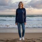 Woman wearing a Deepwater Crew Co. dark navy long-sleeve performance UV hoodie on a beach at sunset.