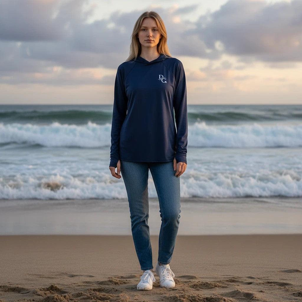 Woman wearing a Deepwater Crew Co. dark navy long-sleeve performance UV hoodie on a beach at sunset.