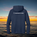Deepwater Crew Co. navy blue performance UV hoodie with white logo on back, set against an ocean sunset background.