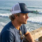 Deepwater Crew Co. navy and white 5-panel trucker cap with embroidered logo worn by a man overlooking the ocean