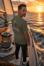 Deepwater Crew Co. olive green 100% cotton t-shirt with graphic print on back, worn by a man on a sailboat at sunset.