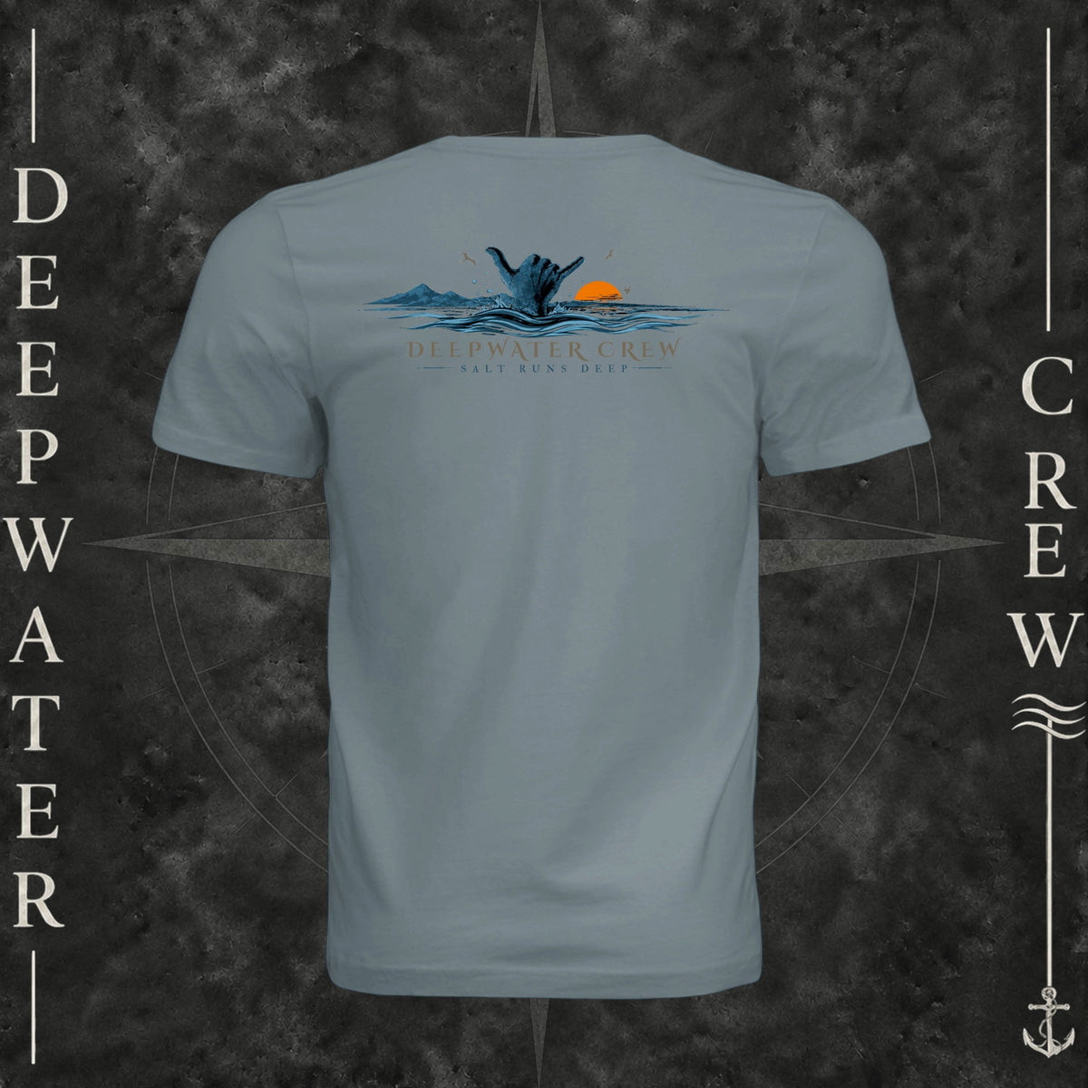 Blue Storm Deepwater Crew Co. Salt Runs Deep crewneck T-shirt, back view with shaka hand, ocean waves, distant mountains, orange sunset, seabirds, and “Salt Runs Deep” lettering.
